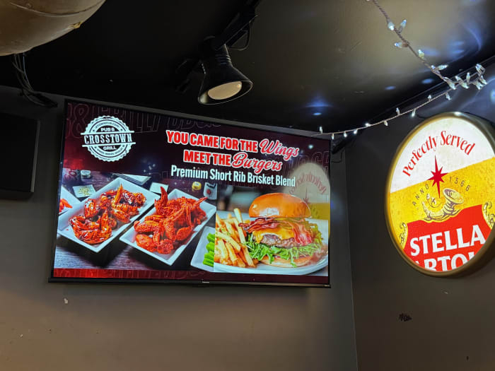 A DDM indoor digital billboard screen actively displaying a local business advertisement inside Crosstown Pub and Grill in Naperville, Illinois